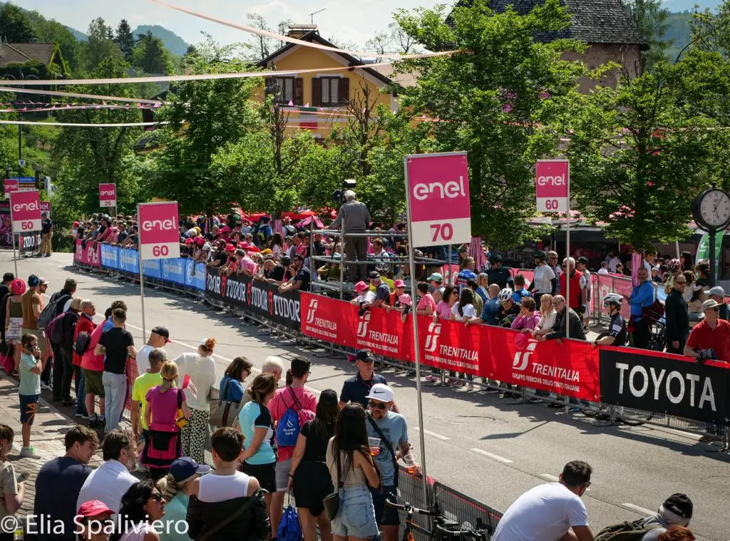 Splende il sole, intanto, in Friuli. Finalmente bel tempo sul Giro inseguito per giorni e giorni dalla pioggia nella sua risalita al Nord; spettacolo fino all’ultimo per una classifica apertissima come non mai. Tantissime le persone sulle strade, a Tarvisio e al Santuario, che applaudono i ciclisti ma soprattutto i due atleti friulani in gara, Alessandro De Marchi e Jonathan Milan, con la sua maglia ciclamino semplicemente passato in 21 tappe da esordiente a eroe acclamato da tutti e protagonista ieri dell’impresa del Giro arrivando in tempo massimo dopo una notte insonne. E poi turisti-tifosi in arrivo da Austria, soprattutto Slovenia per il loro Roglic; telespettatori incollati alle tv da tutto il mondo per assistere al debutto della misteriosa salita del Lussari, musica per le orecchie della Regione (Foto Petrussi)