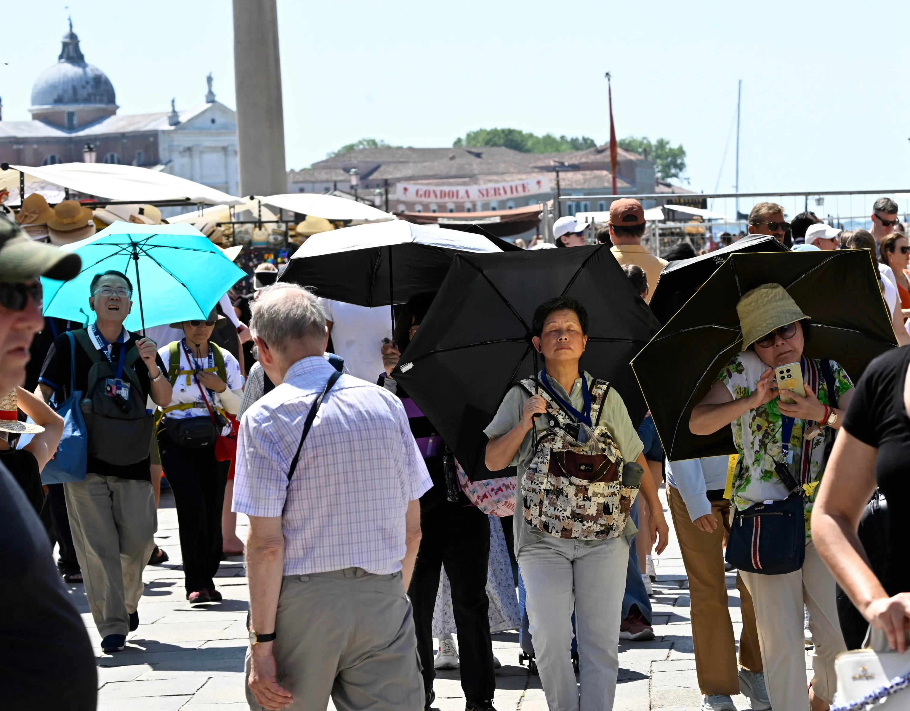 I turisti in piazza San Marco cercano di ripararsi con gli ombrelli. Foto Ansa