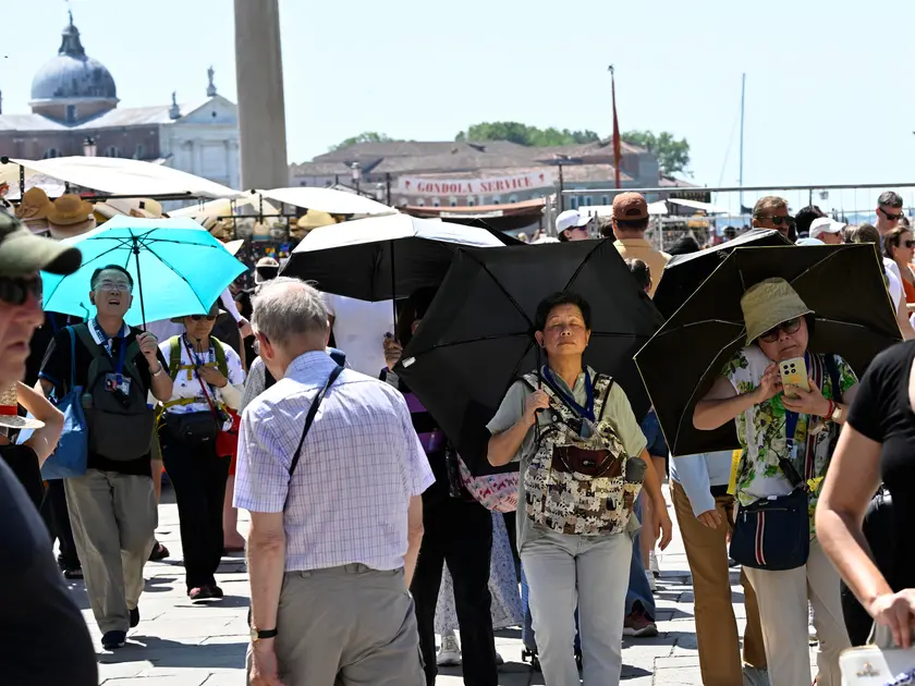I turisti in piazza San Marco cercano di ripararsi con gli ombrelli. Foto Ansa