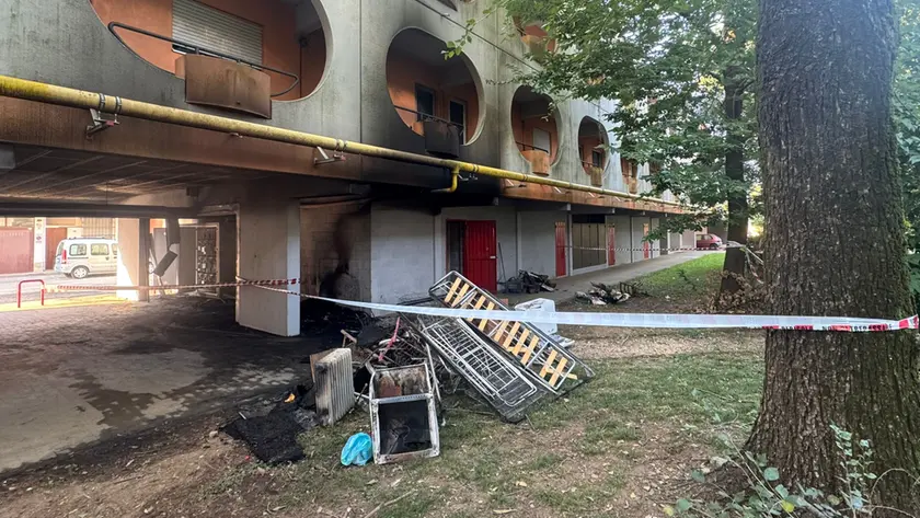 Il materiale incenerito dopo il rogo e i segni dell'incendio sul condominio
