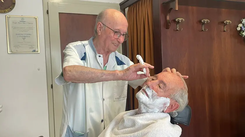 Giovanni Trevisan mentre taglia la barba a un cliente nella sua bottega a Buttrio