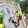 I tecnici della Stazione del Soccorso alpino di Forni di Sopra, imbragati con corde e funi, all’opera per ridipingere l’orologio che guarda a Sud del campanile della chiesa nella frazione di Cella