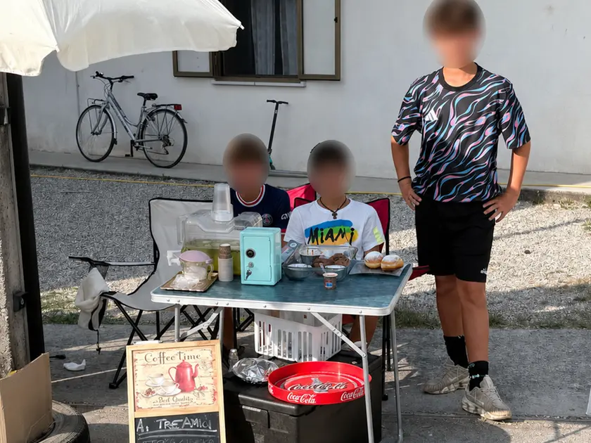 I tre amici dietro al loro banchetto con limonata, caffè e dolcetti