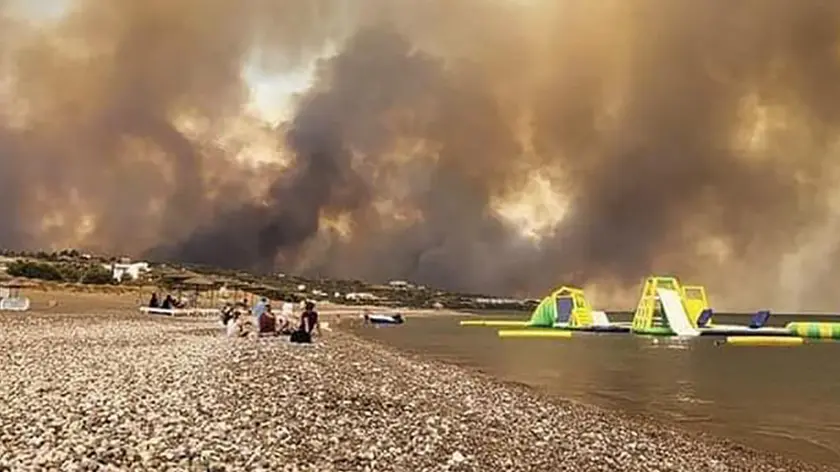 Un’immagine della spiaggia di Rodi minacciata dagli incendi che da giorni si sono sviluppati sull’isola della Grecia