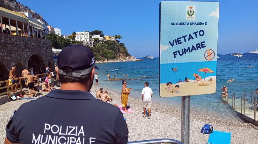 Un agente della polizia municipale controlla la spiaggia dopo che è scattato il divieto di fumo a Capri, 8 agosto 2024. Installati i cartelli e partiti i controlli dopo l'ordinanza del sindaco che vieta di fumare in spiaggia e di abbandonare tutti "rifiuti di prodotti da fumo", questa volta su tutto il territorio comunale. ANSA / GIUSEPPE CATUOGNO