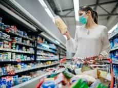 Young person with protective face mask buying groceries/supplies in the supermarket.Preparation for a pandemic quarantine due to coronavirus covid-19 outbreak.Choosing nonperishable food essentials