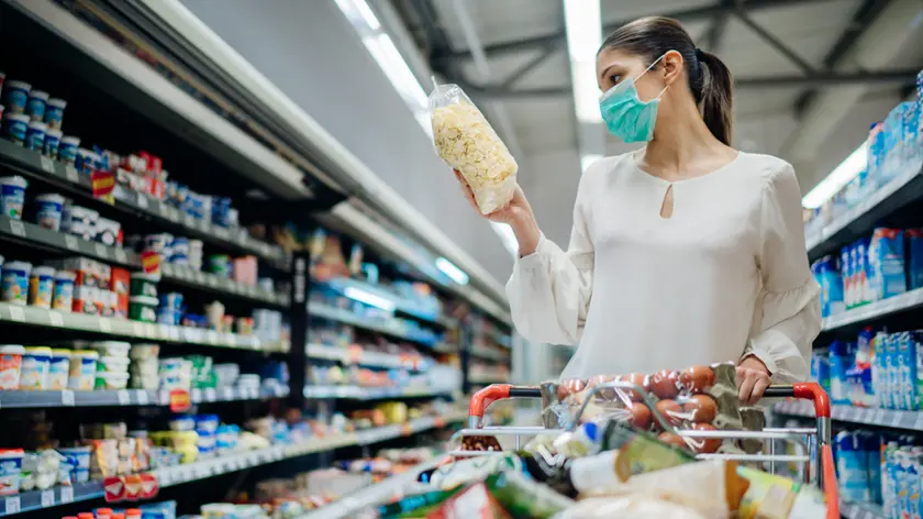 Young person with protective face mask buying groceries/supplies in the supermarket.Preparation for a pandemic quarantine due to coronavirus covid-19 outbreak.Choosing nonperishable food essentials