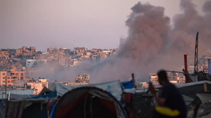 epa11547889 Smoke rises following an Israeli air strike as internally displaced Palestinians sit next to their tents in Khan Younis camp, southern Gaza Strip, 13 August 2024. More than 39,900 Palestinians and over 1,400 Israelis have been killed, according to the Palestinian Health Ministry and the Israel Defense Forces (IDF), since Hamas militants launched an attack against Israel from the Gaza Strip on 07 October 2023, and the Israeli operations in Gaza and the West Bank which followed it. EPA/HAITHAM IMAD