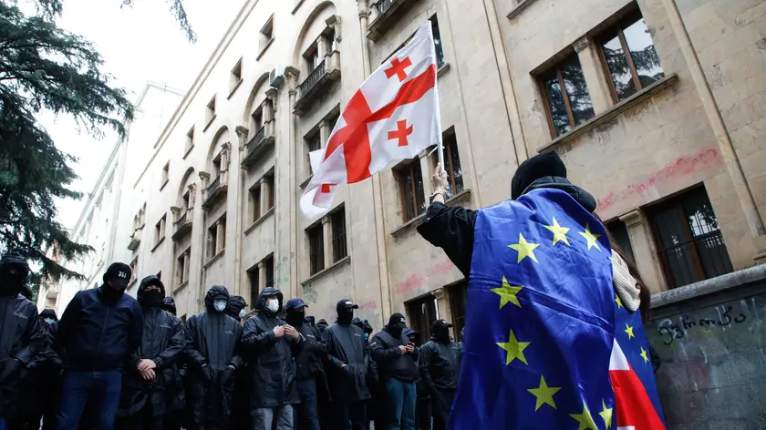 epa11338635 A protester waves a Georgian flag while wearing the European flag in front of policemen blocking a street during a rally against a draft bill on 'foreign agents' near the Parliament building in Tbilisi, Georgia, 14 May 2024. Georgian parliament deputies are set to adopt the law on 'foreign agents' at the plenary session on 14 May, in the third and final reading. Afterwards, the law will be sent to the Georgian president Salome Zourabichvili for signing, who has vowed to veto it. EPA/DAVID MDZINARISHVILI