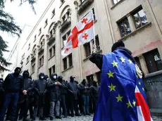 epa11338635 A protester waves a Georgian flag while wearing the European flag in front of policemen blocking a street during a rally against a draft bill on 'foreign agents' near the Parliament building in Tbilisi, Georgia, 14 May 2024. Georgian parliament deputies are set to adopt the law on 'foreign agents' at the plenary session on 14 May, in the third and final reading. Afterwards, the law will be sent to the Georgian president Salome Zourabichvili for signing, who has vowed to veto it. EPA/DAVID MDZINARISHVILI