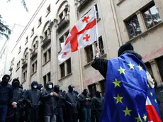 epa11338635 A protester waves a Georgian flag while wearing the European flag in front of policemen blocking a street during a rally against a draft bill on 'foreign agents' near the Parliament building in Tbilisi, Georgia, 14 May 2024. Georgian parliament deputies are set to adopt the law on 'foreign agents' at the plenary session on 14 May, in the third and final reading. Afterwards, the law will be sent to the Georgian president Salome Zourabichvili for signing, who has vowed to veto it. EPA/DAVID MDZINARISHVILI