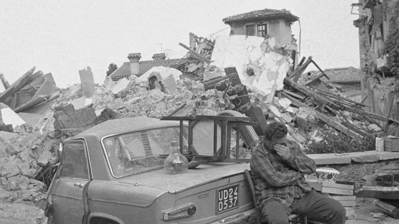 01 May 1976, Udine, Italy --- A man in Udine sits covering his face beside a car crushed by the fallen rubble of a house in Udine. The northern Italian town was shaken by a strong earthquake. --- Image by © Alain Keler/Sygma/CORBIS