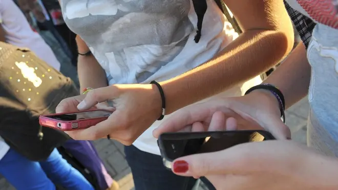 Due ragazze si scambiano messaggi sugli iPhone prima di entrare a scuola.ANSA/FRANCO SILVI