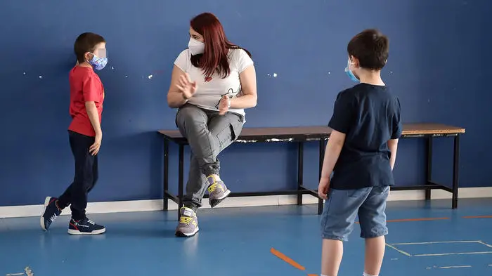 Un' educatrice parla con uno dei bambini delle elementari in una delle tre classi da 4-5 bimbi ciascuna per le elementari, due per i bimbi della materna, allestiti nella palestra e nella ludoteca di Borgosesia di proprietà del Comune, Borgosesia, 12 Maggio 2020. Il servizio di assistenza per bambini da 3 a 10 anni, ideato dal Comune di Borgosesia e da quello di Quarona, è dedicato ai genitori che lavorano e non hanno altre soluzioni per accudire i figli. Controlli della temperatura all'ingresso, banchi distanziatati e zainetto in spalla, i bambini sono affidati a educatori professionali sottoposti a test sierologico, in ambienti sanificati e con accorgimenti che hanno avuto il via libera dall'Unità di Crisi della Regione Piemonte. ANSA/ ALESSANDRO DI MARCO