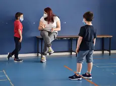 Un' educatrice parla con uno dei bambini delle elementari in una delle tre classi da 4-5 bimbi ciascuna per le elementari, due per i bimbi della materna, allestiti nella palestra e nella ludoteca di Borgosesia di proprietà del Comune, Borgosesia, 12 Maggio 2020. Il servizio di assistenza per bambini da 3 a 10 anni, ideato dal Comune di Borgosesia e da quello di Quarona, è dedicato ai genitori che lavorano e non hanno altre soluzioni per accudire i figli. Controlli della temperatura all'ingresso, banchi distanziatati e zainetto in spalla, i bambini sono affidati a educatori professionali sottoposti a test sierologico, in ambienti sanificati e con accorgimenti che hanno avuto il via libera dall'Unità di Crisi della Regione Piemonte. ANSA/ ALESSANDRO DI MARCO