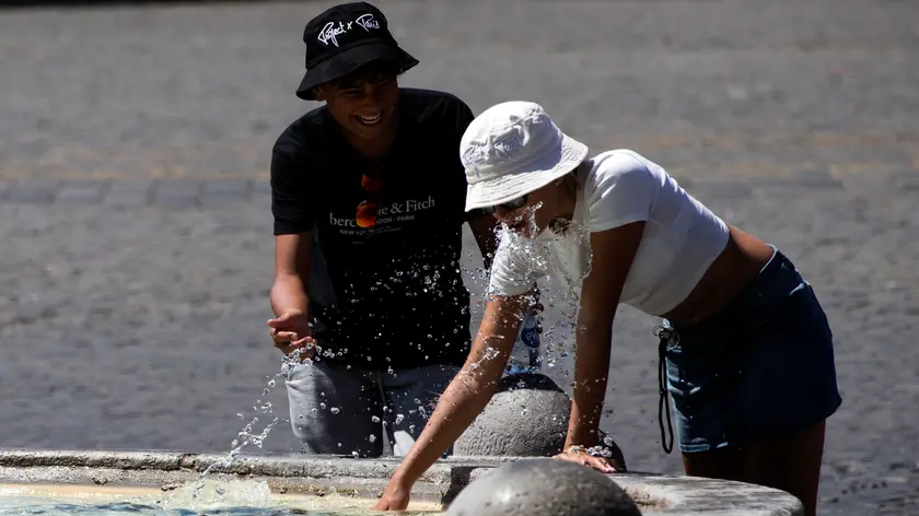Persone si rinfrescano nella fontana di Piazza del Popolo durante l'ondata di caldo, Roma, 19 agosto 2023. ANSA/ANGELO CARCONI