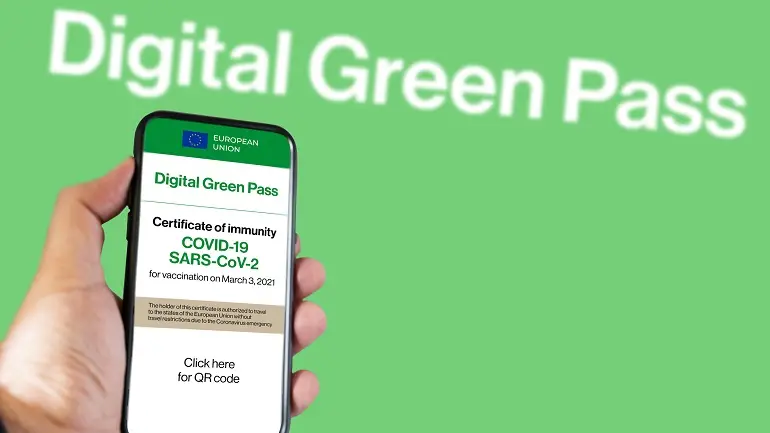 The digital green pass of the european union with the QR code on the screen of a mobile held by a hand with blurred airport in the background. Immunity from Covid-19. Travel without restrictions.