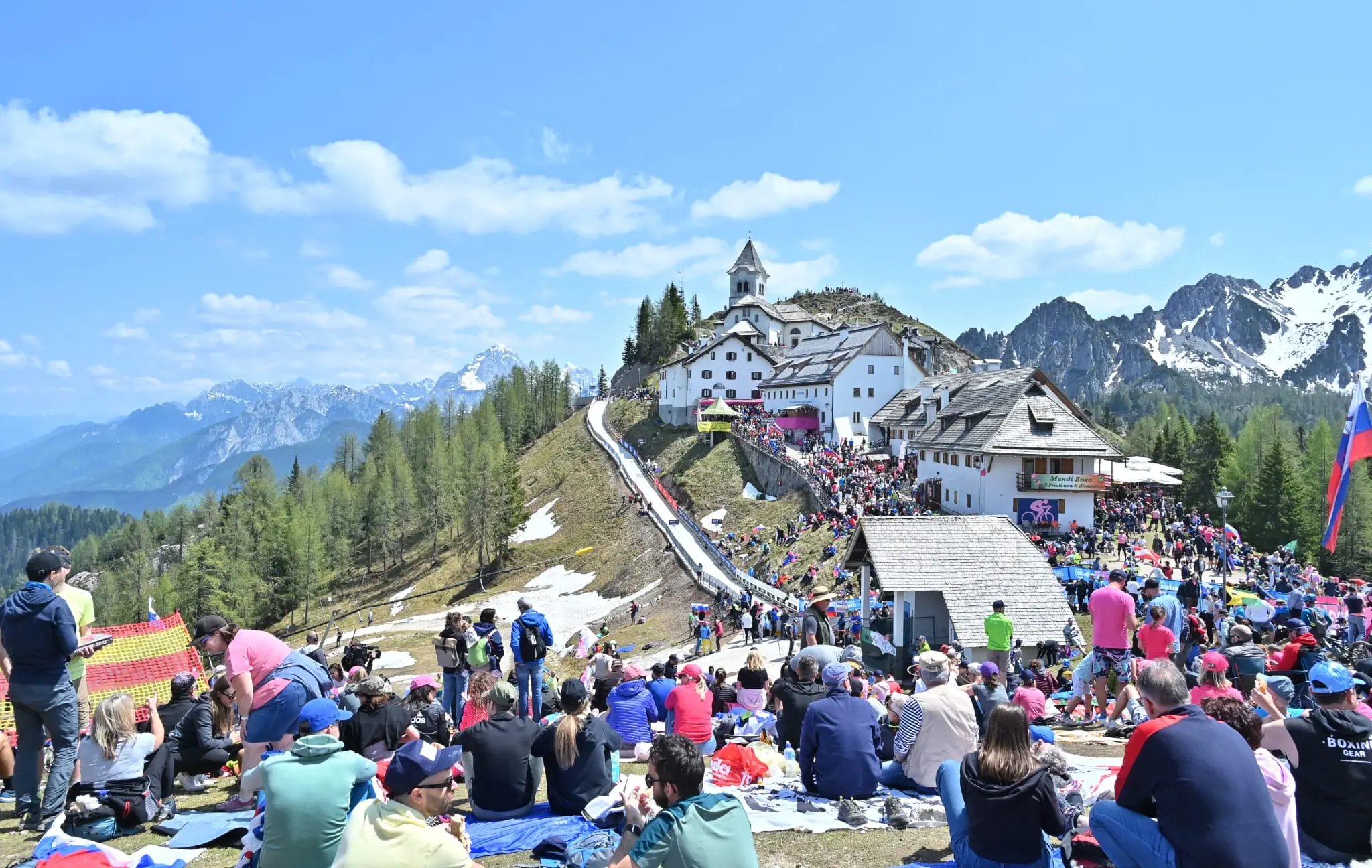 Splende il sole, intanto, in Friuli. Finalmente bel tempo sul Giro inseguito per giorni e giorni dalla pioggia nella sua risalita al Nord; spettacolo fino all’ultimo per una classifica apertissima come non mai. Tantissime le persone sulle strade, a Tarvisio e al Santuario, che applaudono i ciclisti ma soprattutto i due atleti friulani in gara, Alessandro De Marchi e Jonathan Milan, con la sua maglia ciclamino semplicemente passato in 21 tappe da esordiente a eroe acclamato da tutti e protagonista ieri dell’impresa del Giro arrivando in tempo massimo dopo una notte insonne. E poi turisti-tifosi in arrivo da Austria, soprattutto Slovenia per il loro Roglic; telespettatori incollati alle tv da tutto il mondo per assistere al debutto della misteriosa salita del Lussari, musica per le orecchie della Regione (Foto Petrussi)