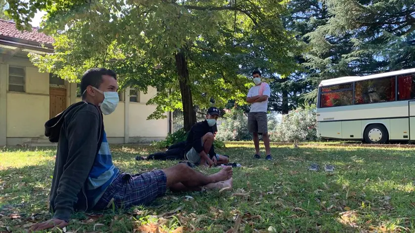 Migranti nordafricani nel giardino dell'ex ospedale psichiatrico di Udine: sullo sfondo uno dei bus che fa da "camera da letto"