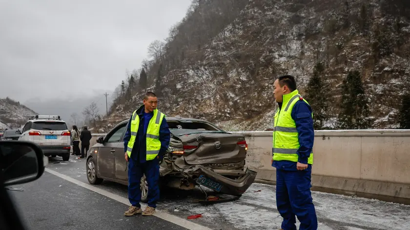 epa11100713 Local security stand guard at a damaged car following an accident caused by slippery roads in Zhenxiong County, Yunnan province southwest of China, 24 January 2024. Local authorities reported at least 31 dead and more than 10 people missing after a landslide hit Liangshui Village in China's southwest province of Yunnan early morning on 22 January. Over 1,000 personnel have been mobilized by the government to help in rescue and evacuation efforts. EPA/MARK R. CRISTINO