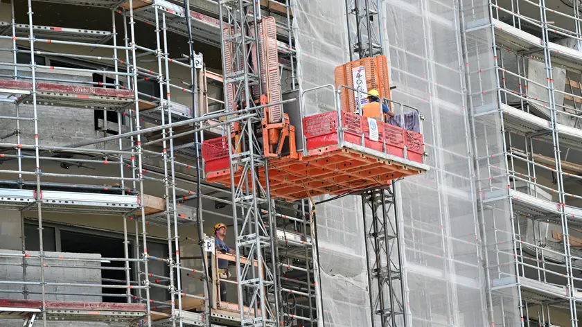 Operai edili al lavoro sulla facciata di un palazzo ricoperto da ponteggi, Milano, 14 giugno 2022. ANSA/DANIEL DAL ZENNARO