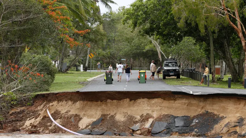 epa11035366 Residents walk near a section of a road that was washed away at the end of Holloways Beach Esplanade in Cairns, Queensland, Australia, 18 December 2023. Residents in far north Queensland are bracing for more rain and further significant flooding. EPA/JOSHUA PRIETO AUSTRALIA AND NEW ZEALAND OUT