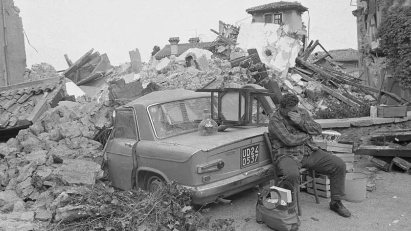 01 May 1976, Udine, Italy --- A man in Udine sits covering his face beside a car crushed by the fallen rubble of a house in Udine. The northern Italian town was shaken by a strong earthquake. --- Image by © Alain Keler/Sygma/CORBIS
