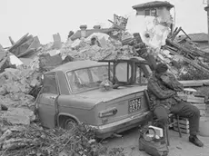 01 May 1976, Udine, Italy --- A man in Udine sits covering his face beside a car crushed by the fallen rubble of a house in Udine. The northern Italian town was shaken by a strong earthquake. --- Image by © Alain Keler/Sygma/CORBIS