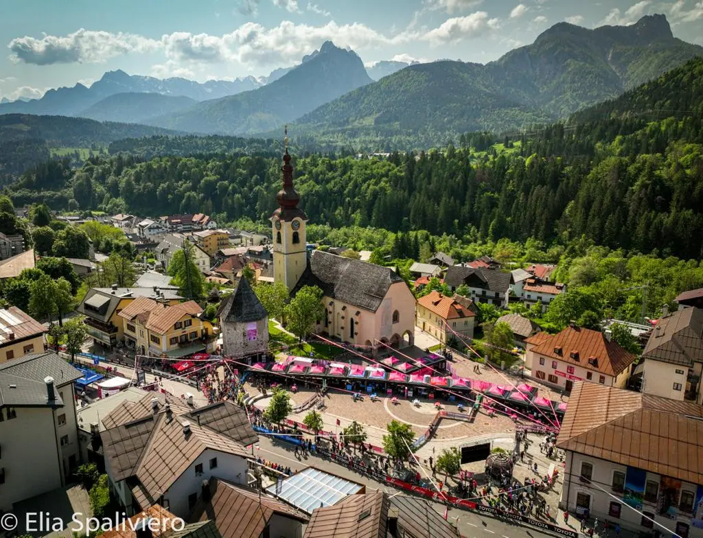 Splende il sole, intanto, in Friuli. Finalmente bel tempo sul Giro inseguito per giorni e giorni dalla pioggia nella sua risalita al Nord; spettacolo fino all’ultimo per una classifica apertissima come non mai. Tantissime le persone sulle strade, a Tarvisio e al Santuario, che applaudono i ciclisti ma soprattutto i due atleti friulani in gara, Alessandro De Marchi e Jonathan Milan, con la sua maglia ciclamino semplicemente passato in 21 tappe da esordiente a eroe acclamato da tutti e protagonista ieri dell’impresa del Giro arrivando in tempo massimo dopo una notte insonne. E poi turisti-tifosi in arrivo da Austria, soprattutto Slovenia per il loro Roglic; telespettatori incollati alle tv da tutto il mondo per assistere al debutto della misteriosa salita del Lussari, musica per le orecchie della Regione (Foto Petrussi)