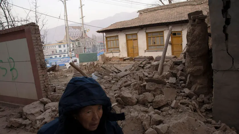 epa11039520 A woman walks past a house damaged by the earthquake in Dahejia, Gansu Province, China, 21 December, 2023. A 6.2 earthquake hit the region on 18 December killing more than 100 people. EPA/ANDRES MARTINEZ CASARES