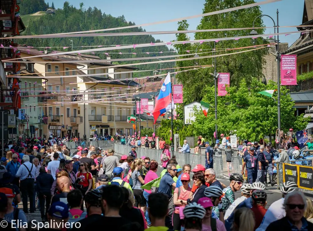 Splende il sole, intanto, in Friuli. Finalmente bel tempo sul Giro inseguito per giorni e giorni dalla pioggia nella sua risalita al Nord; spettacolo fino all’ultimo per una classifica apertissima come non mai. Tantissime le persone sulle strade, a Tarvisio e al Santuario, che applaudono i ciclisti ma soprattutto i due atleti friulani in gara, Alessandro De Marchi e Jonathan Milan, con la sua maglia ciclamino semplicemente passato in 21 tappe da esordiente a eroe acclamato da tutti e protagonista ieri dell’impresa del Giro arrivando in tempo massimo dopo una notte insonne. E poi turisti-tifosi in arrivo da Austria, soprattutto Slovenia per il loro Roglic; telespettatori incollati alle tv da tutto il mondo per assistere al debutto della misteriosa salita del Lussari, musica per le orecchie della Regione (Foto Petrussi)