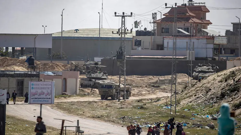 epa11198263 Israeli tanks on patrol (background) as internally displaced Palestinians walk after the Israeli army told residents of the Hamad area in Khan Yunis to leave their homes and head towards Rafah, near the border with Egypt, southern Gaza Strip, 04 March 2024. The Israeli military stated on 04 March that a humanitarian evacuation corridor was established to allow civilians to exit the area. More than 30,500 Palestinians and over 1,300 Israelis have been killed, according to the Palestinian Health Ministry and the Israel Defense Forces (IDF), since Hamas militants launched an attack against Israel from the Gaza Strip on 07 October 2023, and the Israeli operations in Gaza and the West Bank which followed it. EPA/MOHAMMED SABER