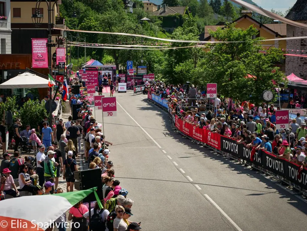 Splende il sole, intanto, in Friuli. Finalmente bel tempo sul Giro inseguito per giorni e giorni dalla pioggia nella sua risalita al Nord; spettacolo fino all’ultimo per una classifica apertissima come non mai. Tantissime le persone sulle strade, a Tarvisio e al Santuario, che applaudono i ciclisti ma soprattutto i due atleti friulani in gara, Alessandro De Marchi e Jonathan Milan, con la sua maglia ciclamino semplicemente passato in 21 tappe da esordiente a eroe acclamato da tutti e protagonista ieri dell’impresa del Giro arrivando in tempo massimo dopo una notte insonne. E poi turisti-tifosi in arrivo da Austria, soprattutto Slovenia per il loro Roglic; telespettatori incollati alle tv da tutto il mondo per assistere al debutto della misteriosa salita del Lussari, musica per le orecchie della Regione (Foto Petrussi)