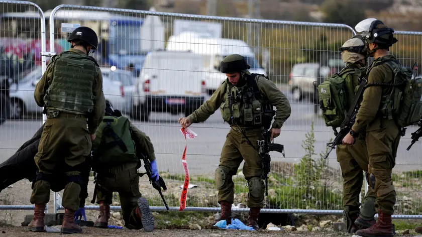 epa05037279 Israeli soldiers pick up debris and bloodied pieces of their investigation at the scene of a Palestinian attack on a bus stop and hitch hiking post outside Efrat in the West Bank settlement block of Gush Etzion, south of Jerusalem, 22 November 2015. A female Israel died from her stabbing wounds inflicted by a Palestinian woman who attacked with a knife. The atacker was shot dead at the scene by Israeli security forces. EPA/JIM HOLLANDER