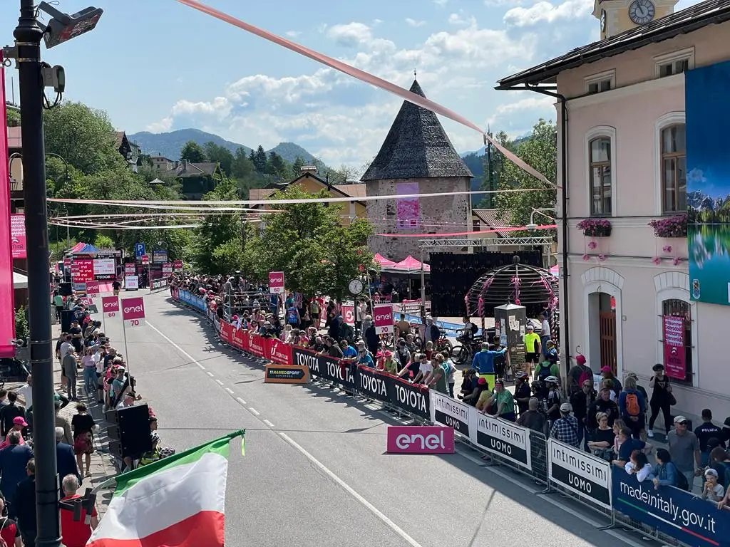 Splende il sole, intanto, in Friuli. Finalmente bel tempo sul Giro inseguito per giorni e giorni dalla pioggia nella sua risalita al Nord; spettacolo fino all’ultimo per una classifica apertissima come non mai. Tantissime le persone sulle strade, a Tarvisio e al Santuario, che applaudono i ciclisti ma soprattutto i due atleti friulani in gara, Alessandro De Marchi e Jonathan Milan, con la sua maglia ciclamino semplicemente passato in 21 tappe da esordiente a eroe acclamato da tutti e protagonista ieri dell’impresa del Giro arrivando in tempo massimo dopo una notte insonne. E poi turisti-tifosi in arrivo da Austria, soprattutto Slovenia per il loro Roglic; telespettatori incollati alle tv da tutto il mondo per assistere al debutto della misteriosa salita del Lussari, musica per le orecchie della Regione (Foto Petrussi)