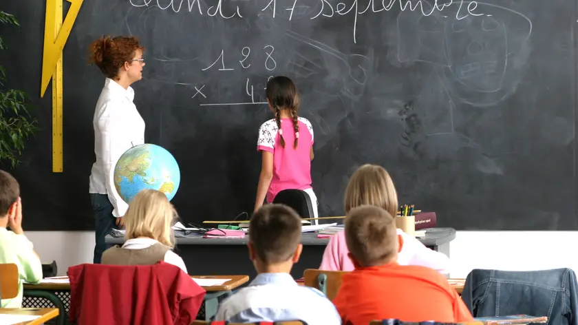 intérieur salle de classe, institutrice regardant fillette de dos au tableau, faisant multiplication, garçons et fillettes assis au 1er plan