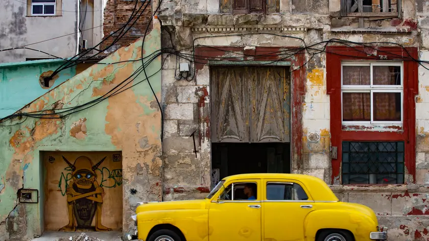 epa11057110 An old automobile in front of a run-down building in Havana, Cuba, 04 January 2024. Cuba is well known for oldtimer cars. EPA/Yander Zamora