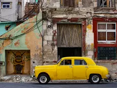 epa11057110 An old automobile in front of a run-down building in Havana, Cuba, 04 January 2024. Cuba is well known for oldtimer cars. EPA/Yander Zamora