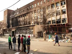 epa10832893 People stand in front of the gutted 80 Albert Street building, where at least 73 people died in a fire, in downtown Johannesburg, South Africa, 01 September 2023. According to Emergency Management Services spokesman Robert Mulaudzi, at least 73 people have died and 52 people were injured in a building fire early morning on 31 August. An investigation into the cause of the fire has been opened as mopping-up operations continue throughout the day. EPA/KIM LUDBROOK