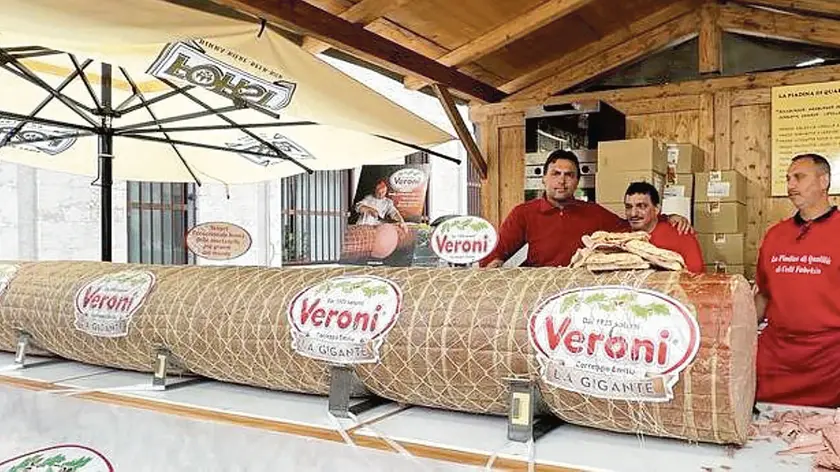 La mortadella, lunga cinque metri e pesante nove quintali, con i gestori dello stand allestito in piazza Duomo in occasione dell’Adunata
